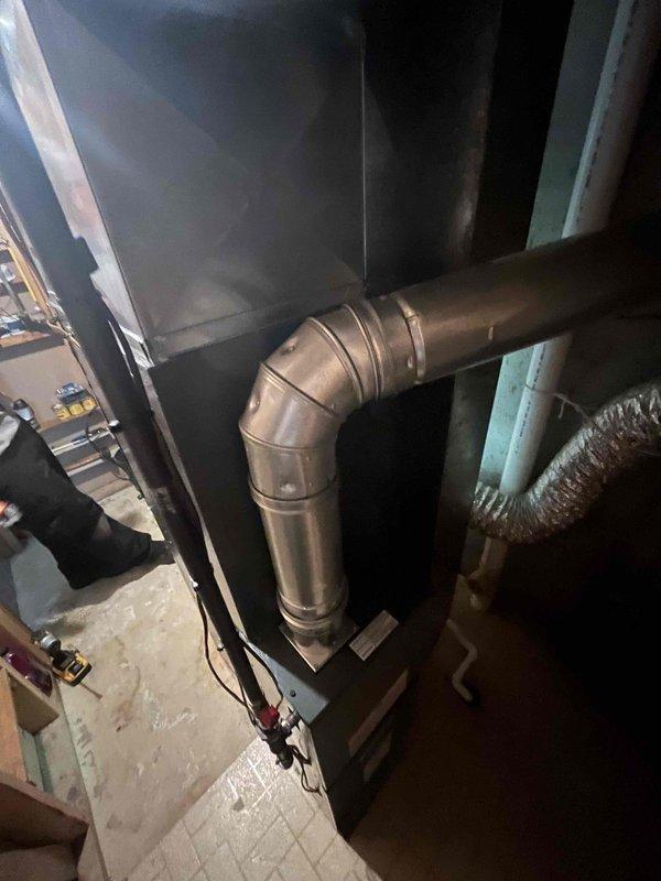 Completed full air conditioning system replacement in residential basement utility room. Removed existing AC unit and installed new high-efficiency furnace with proper venting and drainage systems. Connected galvanized metal ductwork with 90-degree elbow joint to air handler unit, ensuring secure connections and proper airflow. Installed black flexible condensate line and white PVC drainage piping for condensate removal. Verified all electrical connections, safety labels, and warning stickers properly affixed to unit. Tested system operation to confirm proper functionality of new equipment.