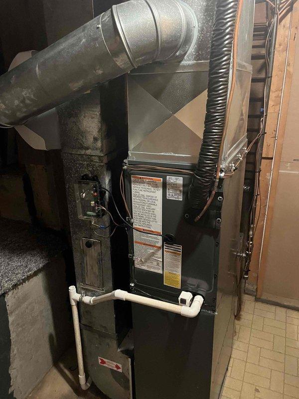 Completed full air conditioning system replacement in residential basement utility room. Removed existing AC unit and installed new high-efficiency furnace with proper venting and drainage systems. Connected galvanized metal ductwork with 90-degree elbow joint to air handler unit, ensuring secure connections and proper airflow. Installed black flexible condensate line and white PVC drainage piping for condensate removal. Verified all electrical connections, safety labels, and warning stickers properly affixed to unit. Tested system operation to confirm proper functionality of new equipment.