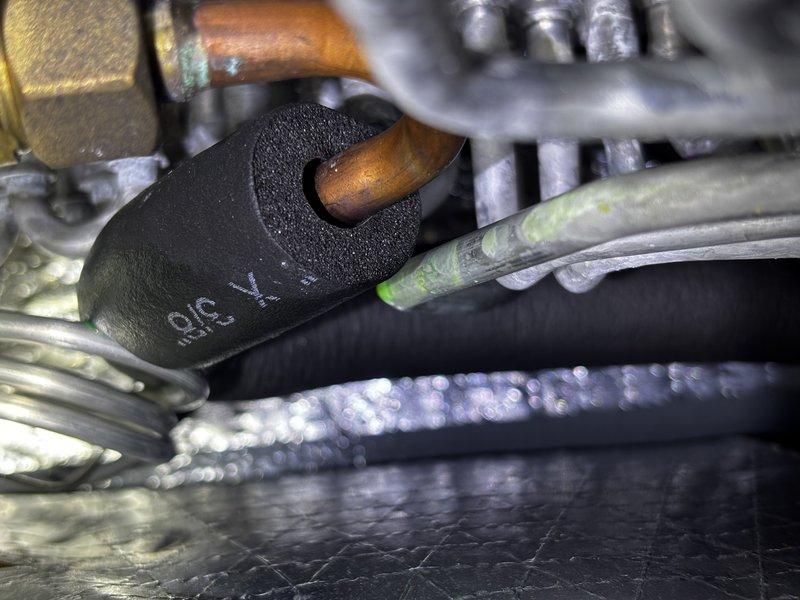 Returned to property to inspect for refrigerant leak following UV dye installation from previous visit. Customer reported decreased cooling ability since initial service. Using UV light inspection, identified active refrigerant leak at copper pipe fitting connection on evaporator coil assembly. Fluorescent dye tracer clearly visible under blacklight illumination, confirming leak location at brazed joint. Documented findings with standard and UV photography showing leak point concentration on refrigerant line connection.