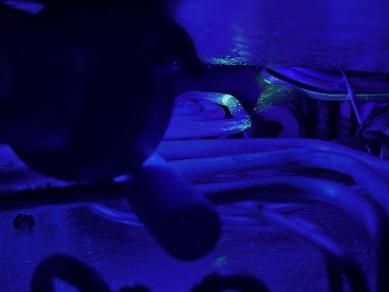 Returned to property to inspect for refrigerant leak following UV dye installation from previous visit. Customer reported decreased cooling ability since initial service. Using UV light inspection, identified active refrigerant leak at copper pipe fitting connection on evaporator coil assembly. Fluorescent dye tracer clearly visible under blacklight illumination, confirming leak location at brazed joint. Documented findings with standard and UV photography showing leak point concentration on refrigerant line connection.