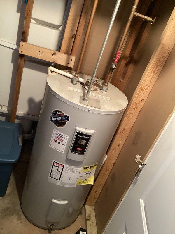 Responded to complaint of toilet tank not fully draining on first flush, an issue present since installation several years ago in 65-year-old home. Upon inspection, observed dual-flush toilet mechanism with blue-tinted water in tank and two yellow float devices connected by tubing. Examined internal flush valve, fill valve, and flapper assembly for proper operation and adjustment. Photographed tank components and related plumbing system including water heater installation to document existing conditions. Advised customer on findings and available options for resolving incomplete flush cycle.