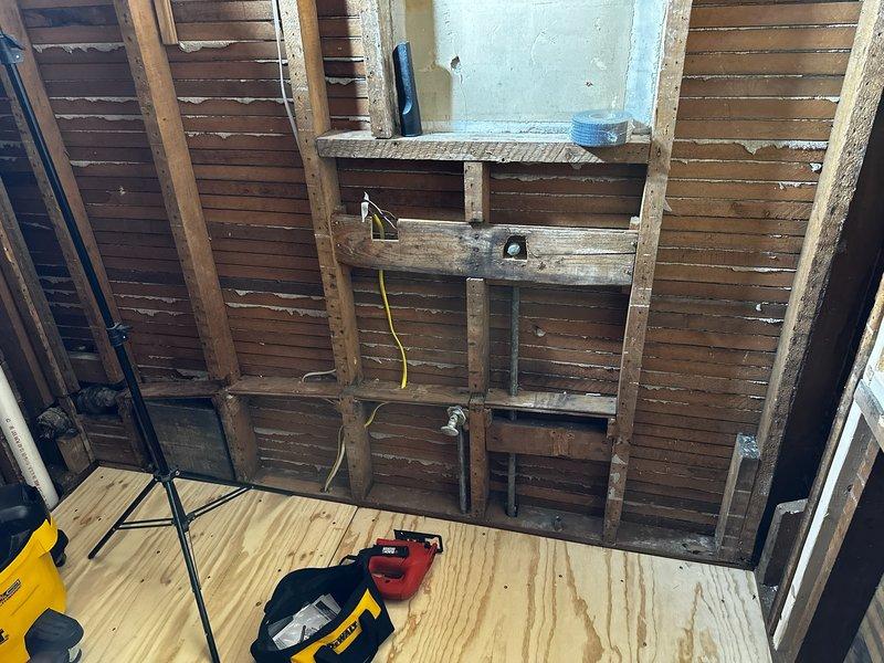 Conducted on-site plumbing estimate for bathroom renovation project requiring complete rough-in installation for toilet, shower, and sink fixtures. Documented existing conditions including exposed wall framing with aged wooden studs and lath boards, open floor structure with accessible crawl space below, and current mechanical infrastructure including galvanized HVAC ductwork and existing PVC drainage lines. Assessed routing requirements for new supply and waste lines through floor joists and wall cavities to accommodate three-fixture bathroom layout, evaluating connection points to existing plumbing system visible in crawl space and determining optimal pipe paths to minimize structural modifications while ensuring proper drainage slope and code compliance.