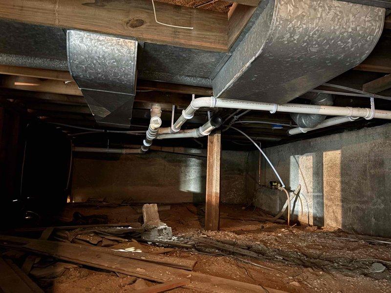Conducted on-site plumbing estimate for bathroom renovation project requiring complete rough-in installation for toilet, shower, and sink fixtures. Documented existing conditions including exposed wall framing with aged wooden studs and lath boards, open floor structure with accessible crawl space below, and current mechanical infrastructure including galvanized HVAC ductwork and existing PVC drainage lines. Assessed routing requirements for new supply and waste lines through floor joists and wall cavities to accommodate three-fixture bathroom layout, evaluating connection points to existing plumbing system visible in crawl space and determining optimal pipe paths to minimize structural modifications while ensuring proper drainage slope and code compliance.
