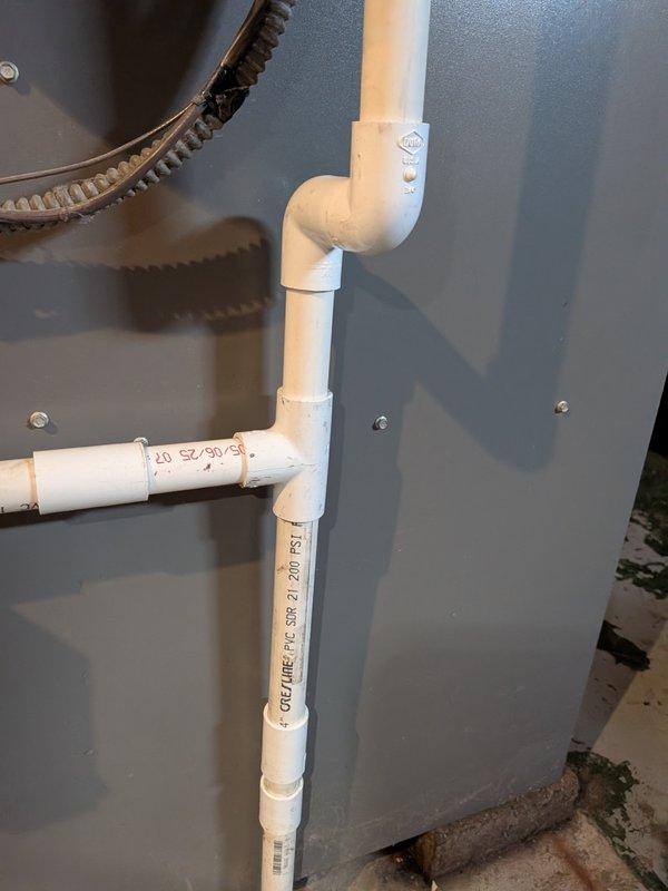 Responded to water leak complaint at furnace location. Upon inspection, identified leak originating from condensate drain system on 20-year-old furnace unit. Examined white PVC drain piping configuration including vertical and horizontal sections with multiple 90-degree elbows. Verified all pipe joints and couplings for proper connection and seal integrity. System appeared to be functioning correctly at time of inspection with no active leaking observed. Piping showed normal wear consistent with age but remained structurally sound. Documented existing drain line configuration and condition with photographs for service records.