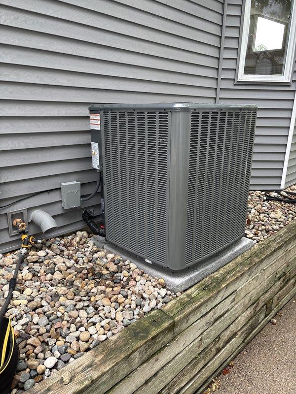 Completed full HVAC system replacement including outdoor condensing unit and indoor air handler/furnace. Installed new dark gray condenser on existing rock pad against exterior wall with proper clearances maintained. Mounted electrical disconnect box and ran refrigerant line sets with appropriate insulation. Interior installation included new furnace unit with integrated ductwork connections, PVC venting system with proper slope and termination, and Aprilaire humidifier mounted to supply plenum. Verified all electrical connections, tested system operation across all modes, confirmed proper refrigerant charge and airflow, and ensured humidity control integration. System commissioned and left in full operational status.