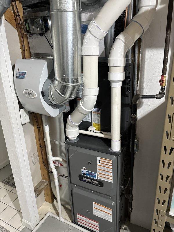 Completed full HVAC system replacement including outdoor condensing unit and indoor air handler/furnace. Installed new dark gray condenser on existing rock pad against exterior wall with proper clearances maintained. Mounted electrical disconnect box and ran refrigerant line sets with appropriate insulation. Interior installation included new furnace unit with integrated ductwork connections, PVC venting system with proper slope and termination, and Aprilaire humidifier mounted to supply plenum. Verified all electrical connections, tested system operation across all modes, confirmed proper refrigerant charge and airflow, and ensured humidity control integration. System commissioned and left in full operational status.