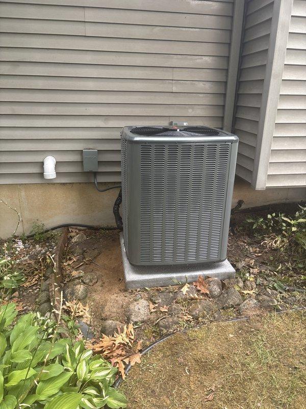 Completed full HVAC system replacement including furnace and air conditioning condenser unit. Installed new gray metal furnace with ENERGY branding in basement utility area with proper venting using white PVC piping and connected metallic ductwork. Mounted Aprilaire humidifier unit to system for enhanced indoor air quality control. Positioned new outdoor AC condenser unit on composite pad against exterior wall with beige vinyl siding, secured electrical conduit and disconnect box to building exterior, and installed condensate drain line. Verified all connections, tested system operation, and confirmed proper airflow throughout installation. System fully operational and ready for service.
