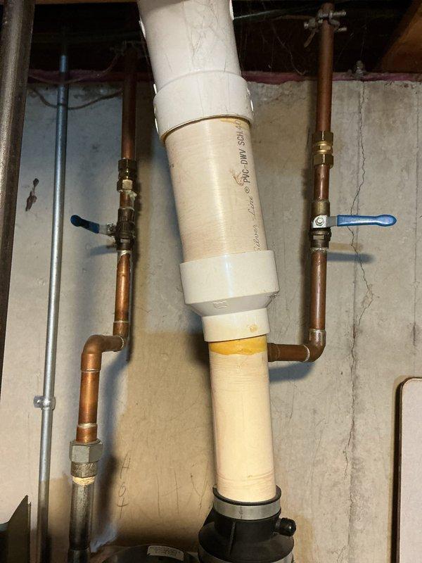Completed estimate for water heater replacement in basement utility area. Assessed existing black cylindrical water heater with copper supply lines, PVC venting system, and associated shut-off valves mounted against concrete block wall. Documented current plumbing configuration including hot and cold water connections with brass fittings, blue and black-handled isolation valves, white PVC drain line, and rubber coupling connections at base. Photographed installation layout and clearance requirements for equipment replacement recommendation.