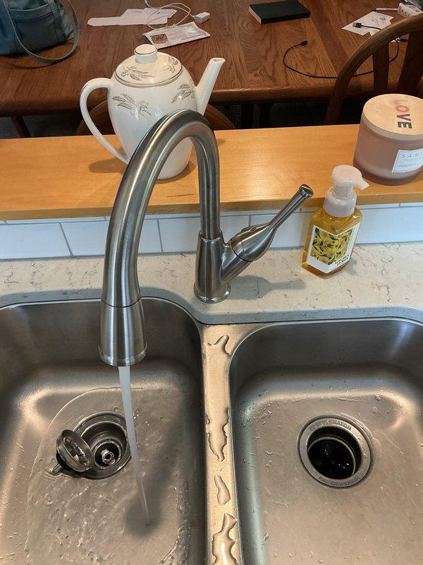 Completed installation of customer-supplied kitchen faucet on double-basin stainless steel sink. Removed existing faucet, installed new high-arc pull-down spray faucet with brushed metal finish, connected hot and cold water supply lines to existing copper piping with brass fittings and shut-off valves, tested for leaks, and verified proper operation of spray head functionality.