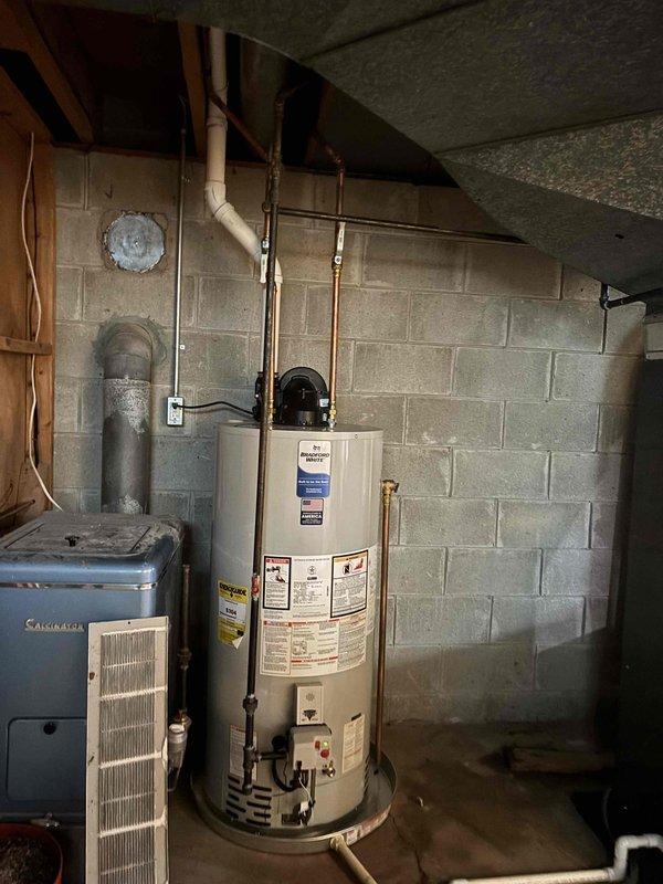 Completed full HVAC system installation including furnace, air conditioning unit, and 50-gallon Bradford White natural gas water heater (Model BG1FV50S6N19) in basement utility area. All equipment installed per manufacturer specifications with proper venting, copper and PVC piping connections, and exhaust systems routed through concrete block wall penetrations. System tested and verified operational with all safety labels intact and accessible for future reference.