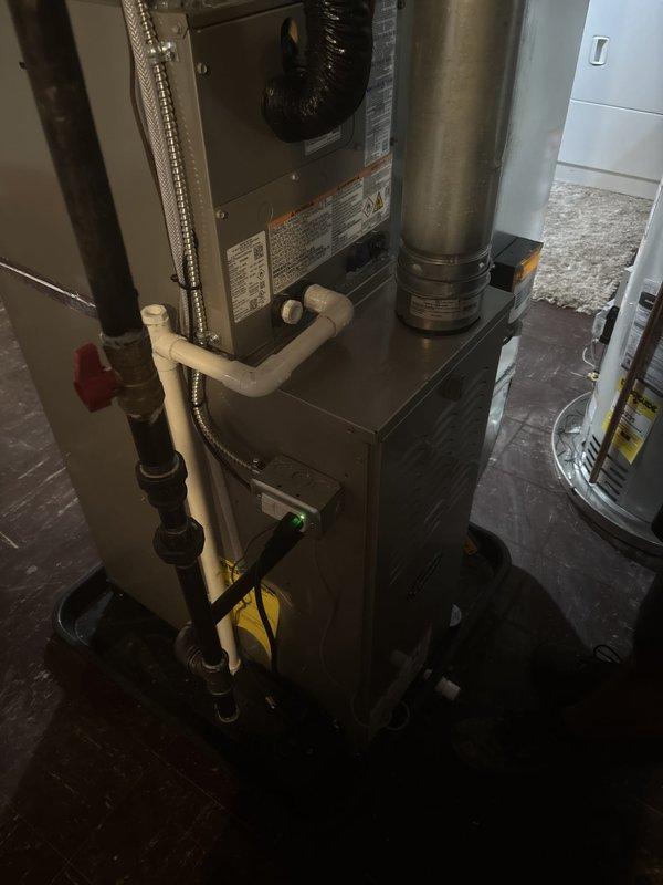 Completed full HVAC system installation including new furnace, air conditioning unit, and water heater in residential basement utility area. All ductwork connections secured and tested, including vertical metal supply ducts and flexible return air ducting. PVC condensate drainage lines installed with proper pitch and gas supply lines connected with shutoff valve. All equipment positioned for optimal airflow and service accessibility, with manufacturer specifications verified and system commissioned for operation.
