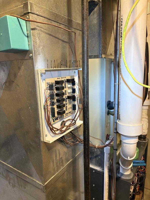 Responded to no cooling call for residential HVAC system with 22-year-old air conditioner and 16-year-old Amana furnace. Inspected basement mechanical room installation including electrical panel, EWC Ultra Zone Control System (Model EWC-ST-2D), condensate drainage assembly, and refrigerant line set. Documented existing two-zone motor control system with relay modules and terminal connections, along with current equipment configuration and electrical components mounted on utility room wall.