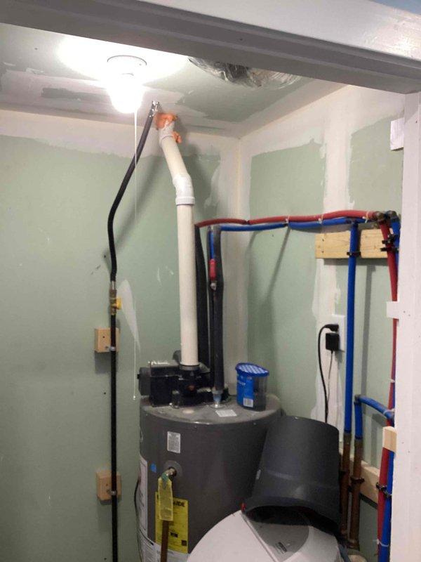 Responded to service call for leaking water heater in residential utility room. Performed comprehensive assessment of existing gray cylindrical water heater showing signs of active leakage. Documented current installation including PVC venting system with 90-degree elbow configuration, PEX manifold distribution system with separate hot and cold water lines, and existing water treatment equipment. Provided detailed estimate for complete water heater replacement to resolve leak issue and restore reliable domestic hot water service.