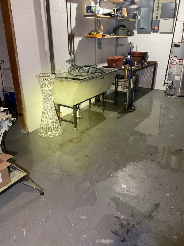 Responded to emergency call for basement drain clog with active flooding. Upon arrival, found extensive standing water throughout basement utility room, with water several inches deep covering concrete floor and affecting storage areas. Located main floor drain with blockage causing backup and overflow. Cleared obstruction from drain line to restore proper drainage flow. Verified water was draining correctly through system after clearing blockage. Documented pre-existing water damage conditions including floor saturation and wall staining from the flooding event.