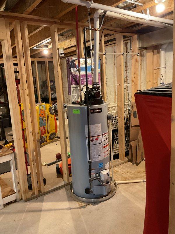 Provided estimate for water heater replacement in unfinished basement with exposed framing and existing mechanical systems. Documented current water heater installation including connections to PVC vent piping routed along ceiling joists and associated plumbing configuration. Assessed installation requirements considering spray foam insulation, HVAC ductwork, and spatial constraints within the construction area for proper equipment access and code-compliant installation.