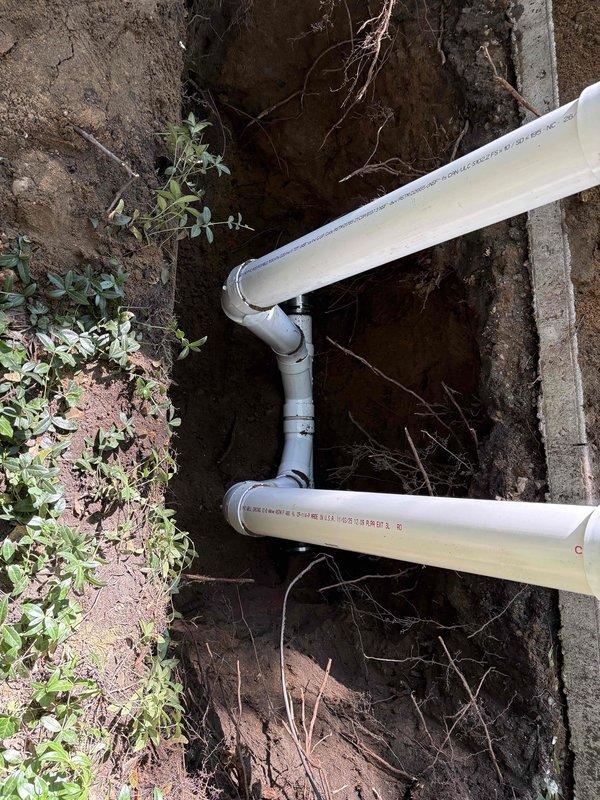 Completed installation of new cleanout access point in existing sewer line system. Excavated trench to expose underground piping, installed white PVC cleanout assembly with gray elbow fittings to provide maintenance access, and performed high-pressure water jetting of the line to clear blockages and restore proper flow. Backfilled and restored work area upon completion.
