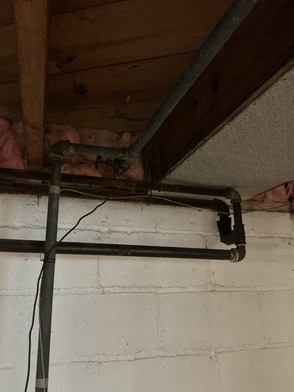 Completed plumbing project estimate for gas line replacement in a 75-year-old single-family residence. Inspected existing black iron gas piping system located in basement crawl space area, documenting current pipe routing, connections, and overall condition of the gas distribution network. Photographed exposed gas lines running horizontally through floor joists, including 90-degree elbow fittings and connection points, to assess scope of replacement work needed for aging gas infrastructure.