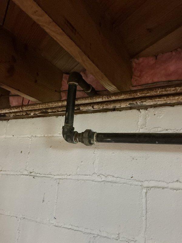 Completed plumbing project estimate for gas line replacement in a 75-year-old single-family residence. Inspected existing black iron gas piping system located in basement crawl space area, documenting current pipe routing, connections, and overall condition of the gas distribution network. Photographed exposed gas lines running horizontally through floor joists, including 90-degree elbow fittings and connection points, to assess scope of replacement work needed for aging gas infrastructure.