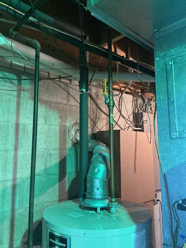 Responded to water leak reported at base of 21-year-old Lennox furnace. Upon inspection, determined leak was originating from condensate pump system rather than furnace unit itself. Photographed mechanical room showing water heater, green-painted piping system, and condensate pump assembly mounted on concrete floor. Examined pump connections and discharge piping for signs of failure or obstruction. Verified furnace heating and cooling functions remained operational despite moisture issue. Documented equipment condition and leak source for further evaluation and repair recommendations.