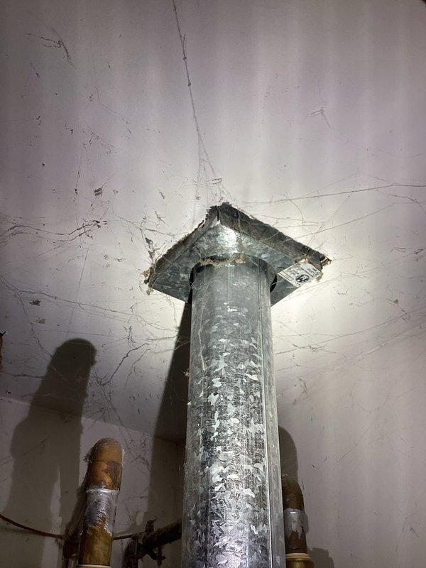 Provided estimate for replacement of existing Ostate brand water heater, approximately 20 years old. Unit is installed in confined utility closet with vertical exhaust venting through ceiling. Existing installation shows significant age with deteriorated vent insulation, cracked wall surfaces, and worn components throughout. Documented current configuration including flexible water supply lines with shut-off valves and existing venting system for replacement specifications.