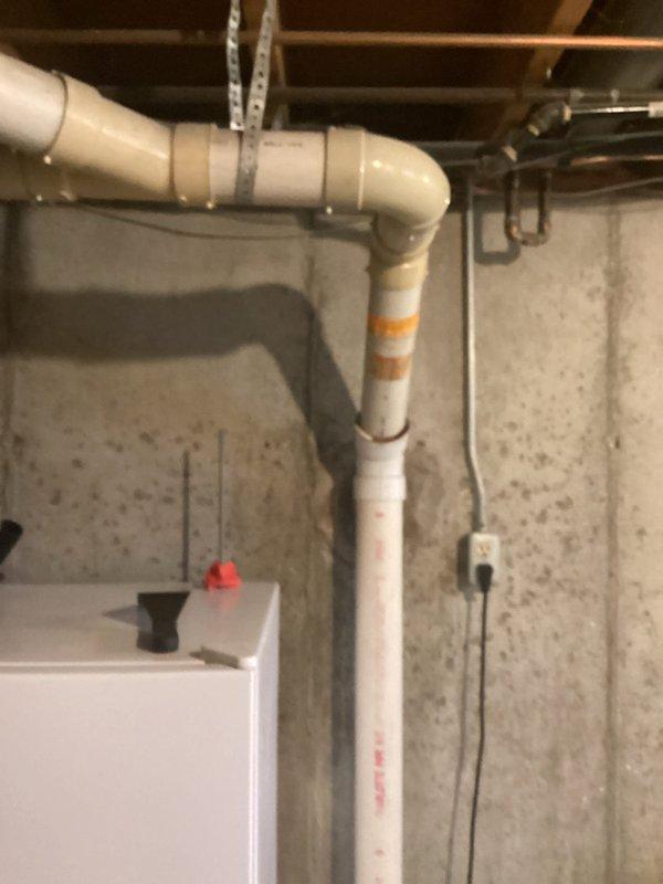 Provided project estimate for connecting water supply line to exterior hose bibb at 50-year-old single-family residence. Assessed existing basement plumbing infrastructure including white PVC drainage system with visible corrosion at pipe joints and connections near floor joists. Evaluated routing options from main water supply to proposed outdoor faucet location, considering existing pipe runs along concrete foundation walls and clearances around water heater. Documented current plumbing configuration and structural conditions to determine materials, labor requirements, and optimal installation pathway for new water supply connection.
