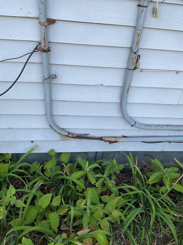 Conducted electrical estimate for century-old home experiencing hazardous conditions with crackling and warm fuse box affecting entire electrical system. Documented exterior electrical service equipment including dual utility meters, weathered conduit system with visible rust and corrosion at connection points, and aging infrastructure requiring comprehensive evaluation for safe electrical panel replacement and service upgrade.
