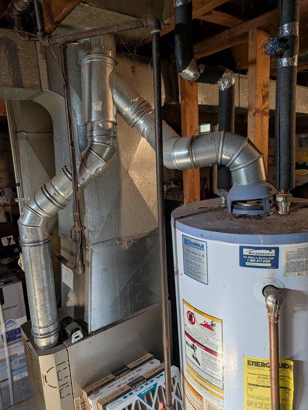Provided estimate for water heater replacement in residential basement utility area. Assessed existing white cylindrical water heater with connected flue piping and adjacent HVAC ductwork system. Documented current equipment specifications and installation configuration for replacement proposal.