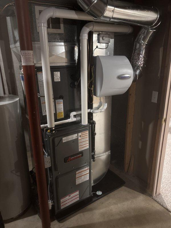 Completed full HVAC system installation including new Amana furnace and outdoor condensing unit. Installed furnace in utility area with proper venting and ductwork connections, mounted Aprilaire humidifier on supply plenum with PVC drain line routed to floor drain. Set outdoor AC condenser on concrete pad between building exterior walls, completed refrigerant line set connections and electrical hookup with disconnect box mounted on siding. Verified all ductwork transitions secure, tested system startup and operation, confirmed proper airflow and temperature differential across coil. Installation meets manufacturer specifications and local code requirements.