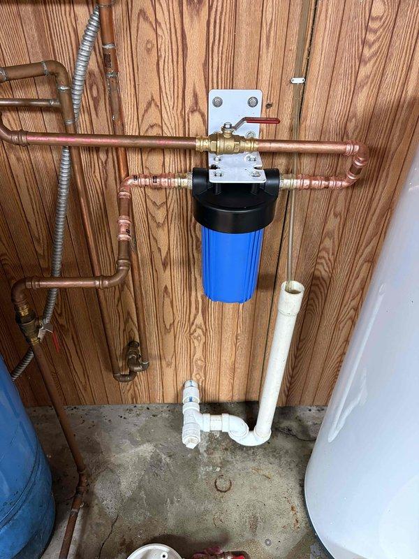 Responded to service call for whole house water filter replacement. Upon arrival, accessed the existing filtration system mounted on basement wall with copper supply lines and shut-off valves. Removed the old filter cartridge from the blue housing canister using appropriate tools. Installed client-provided replacement filter cartridge, ensuring proper seating and seal integrity. Reassembled the filter housing, purged air from the system, and verified all connections were secure with no leaks present. System restored to full operation with improved water flow.