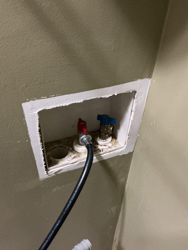 Accessed and serviced washing machine water supply valves recessed in wall cavity. Adjusted hot and cold shut-off valves with red and blue handles for improved accessibility. Verified proper operation of both valves and confirmed secure connections to braided stainless steel supply lines. Ensured access opening was properly maintained for future serviceability.