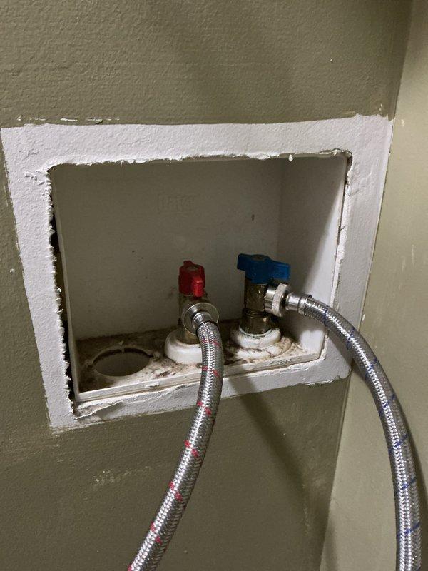 Accessed and serviced washing machine water supply valves recessed in wall cavity. Adjusted hot and cold shut-off valves with red and blue handles for improved accessibility. Verified proper operation of both valves and confirmed secure connections to braided stainless steel supply lines. Ensured access opening was properly maintained for future serviceability.