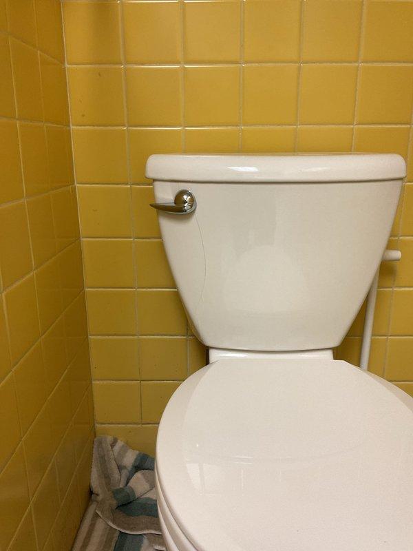 Responded to toilet leak complaint and performed thorough inspection of two-piece toilet fixture with chrome flush handle. Upon examination, documented existing conditions with photographs showing yellow tile wall installation and hexagonal floor tile surrounding fixture. Verified toilet operation and assessed all visible components including tank, bowl, flush mechanism, and base connections for signs of active leakage or water damage.