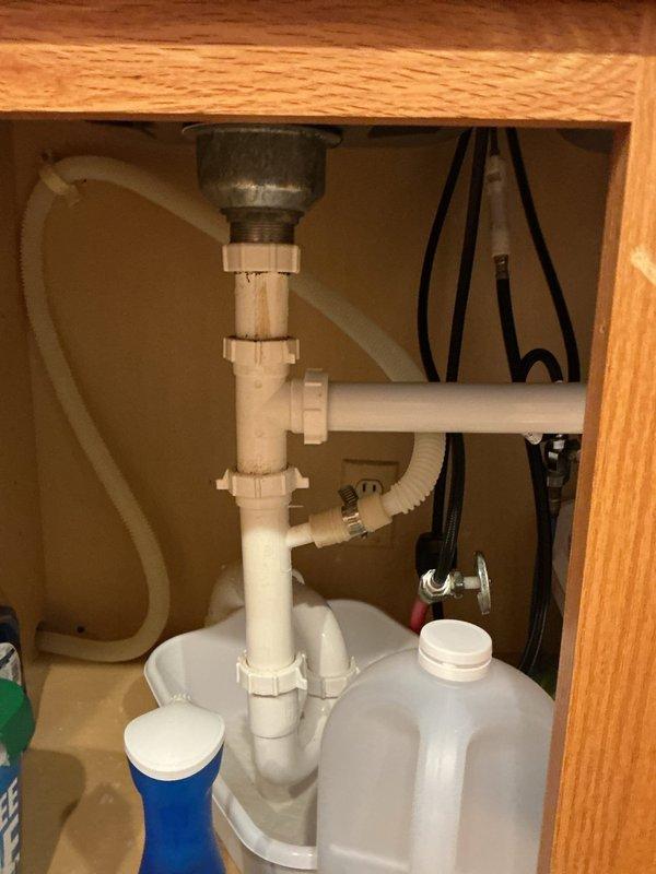 Responded to complaint of sewer-like odor in residence suspected to originate from clogged plumbing vent. Conducted comprehensive inspection of drainage system including under-sink plumbing configuration and rooftop vent stack. Examined kitchen sink drain assembly and PVC waste lines beneath cabinet for proper venting and trap function. Inspected rooftop plumbing vent stack and identified weathered paint condition on vent pipe with deteriorated rubber boot flashing at roof penetration. Documented existing plumbing conditions with photographs for service records. Assessed vent stack for potential blockages or restrictions that could cause negative air pressure and allow sewer gases to enter living space through fixture traps.
