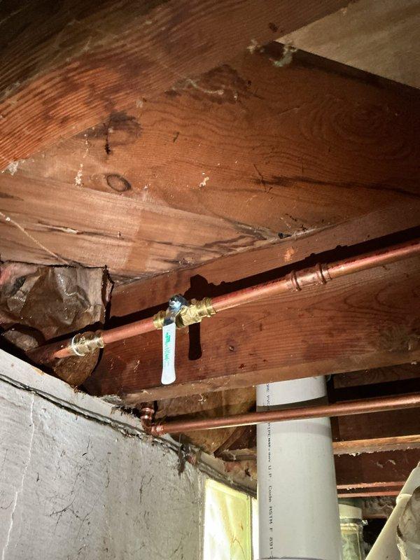 Responded to plumbing leak at copper pipe fitting in basement area that began immediately following recent plumbing installation work. Upon inspection, identified active drip at brass fitting connection point along horizontal copper supply line secured to exposed floor joists. Tightened fitting connection, verified proper seal, and confirmed leak was resolved. Documented existing plumbing configuration including copper supply lines with brass valves, PVC drain piping, and insulation materials in 75-year-old residential structure for service records.