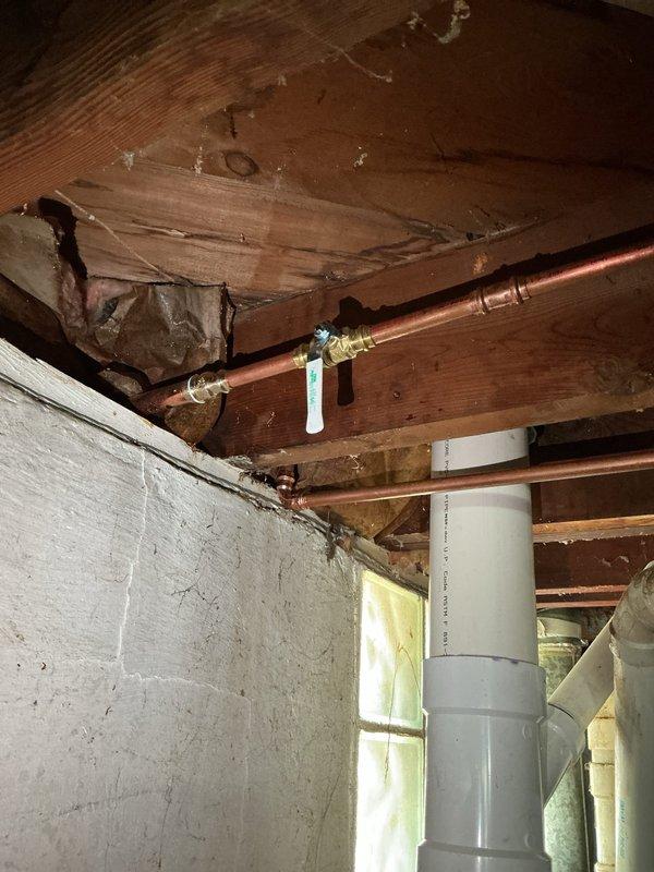 Responded to plumbing leak at copper pipe fitting in basement area that began immediately following recent plumbing installation work. Upon inspection, identified active drip at brass fitting connection point along horizontal copper supply line secured to exposed floor joists. Tightened fitting connection, verified proper seal, and confirmed leak was resolved. Documented existing plumbing configuration including copper supply lines with brass valves, PVC drain piping, and insulation materials in 75-year-old residential structure for service records.