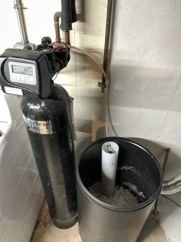 Responded to ongoing water softener issue where salt pellets were converting to mush in brine tank since November 2024. Inspected Peerless water softener system including control head, resin tank, and brine reservoir. Evaluated salt bridge formation and mushing condition in gray brine tank, noting customer had used same salt brand successfully for two years prior without issue. Examined control valve programming, regeneration cycle settings, and brine draw system operation. Assessed water hardness levels and system performance parameters. Photographed installation including digital control head display, plumbing connections, brine tank condition with visible salt media, and utility sink area showing mineral staining indicative of water quality concerns. Discussed findings with customer regarding persistent salt mushing despite previous service attempts by other technician who attributed problem to salt quality. Reviewed system age and repair history, noting this was fourth service call