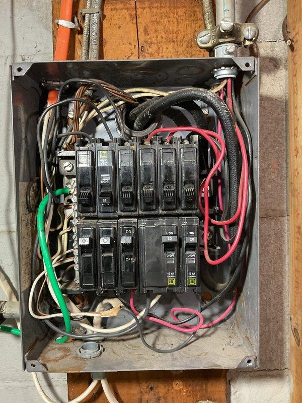 # Electrical Panel Inspection and Power Quality Assessment

Responded to customer complaint of power surges and flickering lights throughout the home, with symptoms worsening when appliances were in operation. Performed comprehensive inspection of main electrical distribution panel and circuit breaker assembly. 

Upon examination, found residential panel box containing eleven total circuit breakers (six upper row, five lower row) with mixed breaker brands including Square D units. Observed disorganized wiring configuration within panel enclosure with multiple conductor loops and coils present. Panel showed signs of age with visible dust accumulation and surface discoloration on metal enclosure.

Inspected all incoming and outgoing circuit conductors including black, white, red, and green insulated wires of various gauges. Verified breaker connections and examined for signs of overheating, loose terminations, or damaged components that could cause intermittent power quality issues. Chec