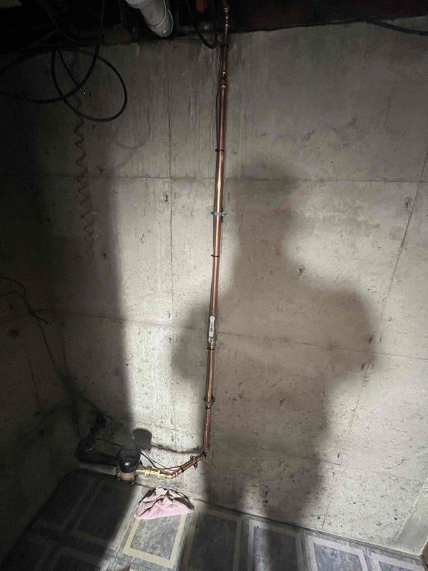 Completed plumbing project installation in basement utility area involving copper pipe installation with proper mounting brackets secured to concrete ceiling. Installed white PVC drainage system with vertical and horizontal runs, properly supported with straps and clips attached to wooden framing members. Coordinated piping routing alongside existing electrical conduit, black flexible tubing, and garage door track system to ensure proper clearances and accessibility for future maintenance.