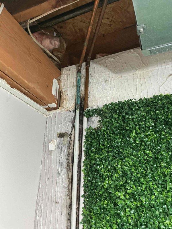 Responded to plumbing leak call at 30-year-old residential property. Upon arrival, performed visual inspection of reported leak area where wall meets ceiling near attic access point. Identified corroded turquoise-colored water supply line running vertically along corner junction, exhibiting rust staining and discoloration at connection points indicative of slow leak. Documented conditions with photographs showing exposed ceiling cavity with wooden framing, insulation, and compromised piping. Recommended pipe replacement due to age-related corrosion and advised customer of warranty coverage options for repair authorization.