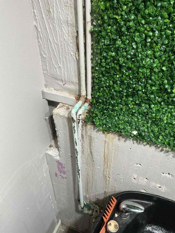 Responded to plumbing leak call at 30-year-old residential property. Upon arrival, performed visual inspection of reported leak area where wall meets ceiling near attic access point. Identified corroded turquoise-colored water supply line running vertically along corner junction, exhibiting rust staining and discoloration at connection points indicative of slow leak. Documented conditions with photographs showing exposed ceiling cavity with wooden framing, insulation, and compromised piping. Recommended pipe replacement due to age-related corrosion and advised customer of warranty coverage options for repair authorization.