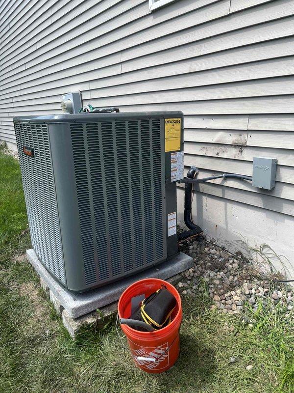 Completed full HVAC system installation including new furnace and air conditioning condenser unit. Installed outdoor AC condenser on concrete pad with proper refrigerant line connections and electrical disconnect, positioned against exterior wall with appropriate clearances. Indoor furnace installation completed in basement mechanical room with integrated Aprilaire air filtration system, new ductwork connections, and PVC condensate drainage lines properly routed and secured.