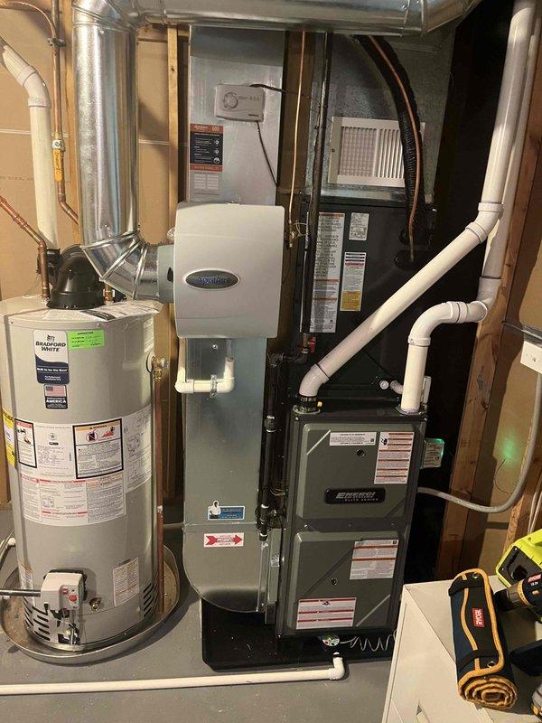 Completed full HVAC system installation including new furnace and air conditioning condenser unit. Installed outdoor AC condenser on concrete pad with proper refrigerant line connections and electrical disconnect, positioned against exterior wall with appropriate clearances. Indoor furnace installation completed in basement mechanical room with integrated Aprilaire air filtration system, new ductwork connections, and PVC condensate drainage lines properly routed and secured.