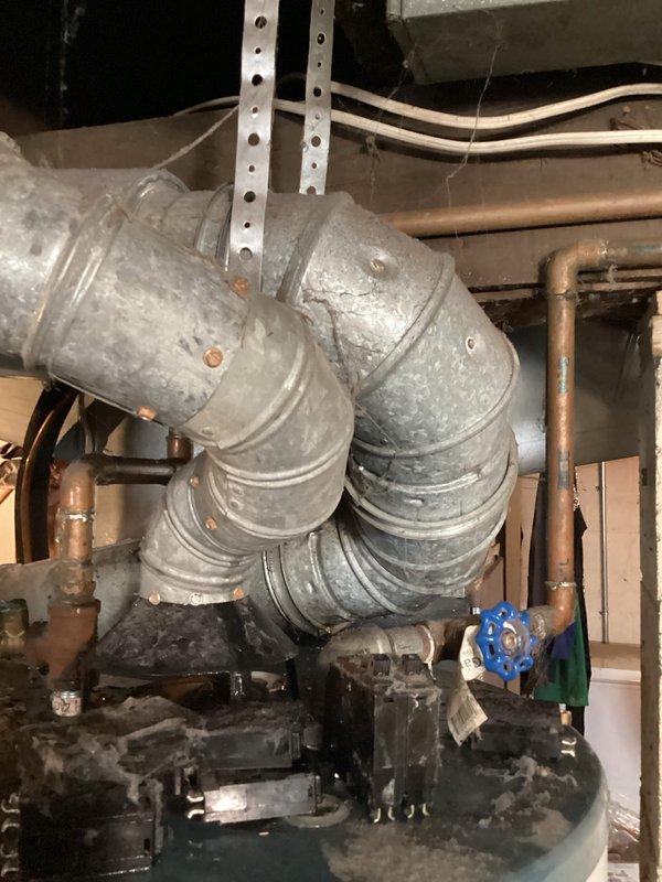 Responded to emergency water leak call for Richmond Integra water heater over 15 years old with active leak reported from top of unit. Upon arrival, inspected water heater and surrounding plumbing connections, including copper supply lines, shut-off valves, and ductwork connections at top of unit. Documented existing conditions with photographs showing water heater installation in basement utility area with overhead ductwork, exposed plumbing, and structural components. Assessed leak source at top connections of aging water heater and provided recommendations for repair or replacement given age of unit exceeding typical service life.