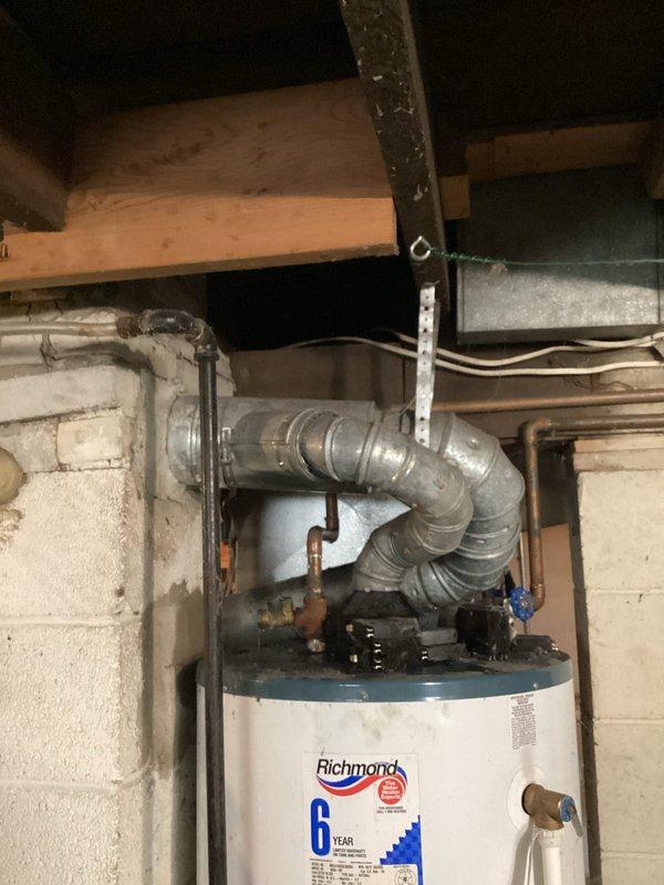 Responded to emergency water leak call for Richmond Integra water heater over 15 years old with active leak reported from top of unit. Upon arrival, inspected water heater and surrounding plumbing connections, including copper supply lines, shut-off valves, and ductwork connections at top of unit. Documented existing conditions with photographs showing water heater installation in basement utility area with overhead ductwork, exposed plumbing, and structural components. Assessed leak source at top connections of aging water heater and provided recommendations for repair or replacement given age of unit exceeding typical service life.