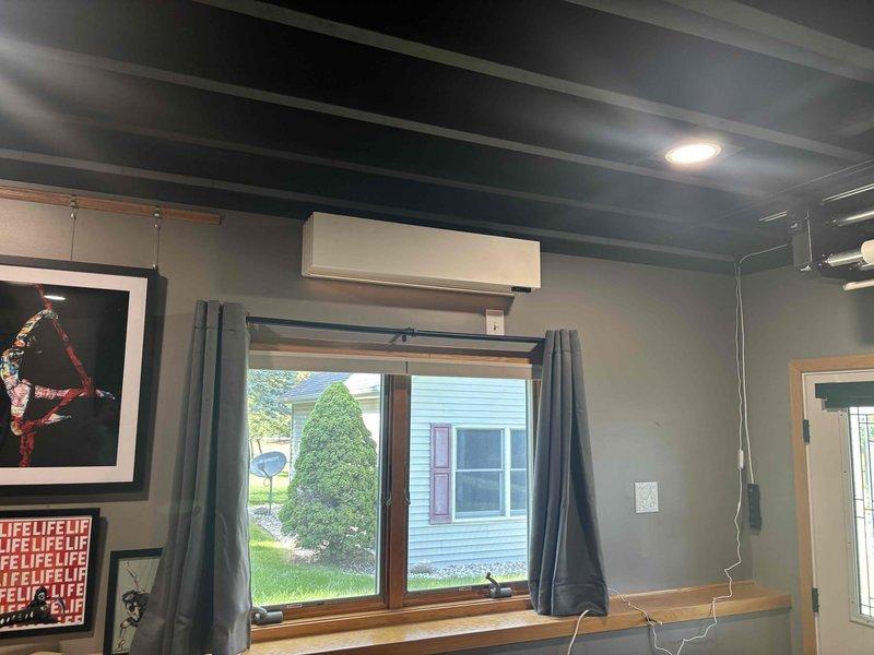 Completed installation of ductless mini-split system including outdoor Quilt brand condenser unit mounted on elevated stand with gravel pad and indoor wall-mounted air handler positioned above window. Installed refrigerant line set, electrical connections, and condensate drainage with all components tested and operational per manufacturer specifications.