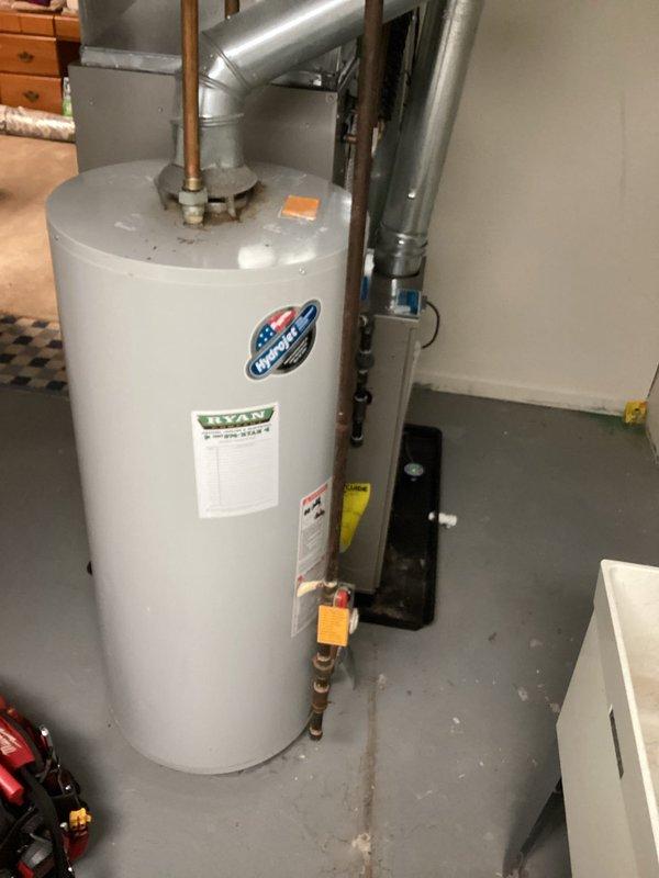 Completed estimate for water heater replacement at 50-year-old residential property. Existing tank-style water heater showing signs of age with visible corrosion and rust staining around pipe connections. Unit located in basement mechanical room alongside furnace system with copper supply lines, brass fittings, and metallic venting in place. Documented current installation configuration and confirmed customer contact information for future coordination of replacement work.