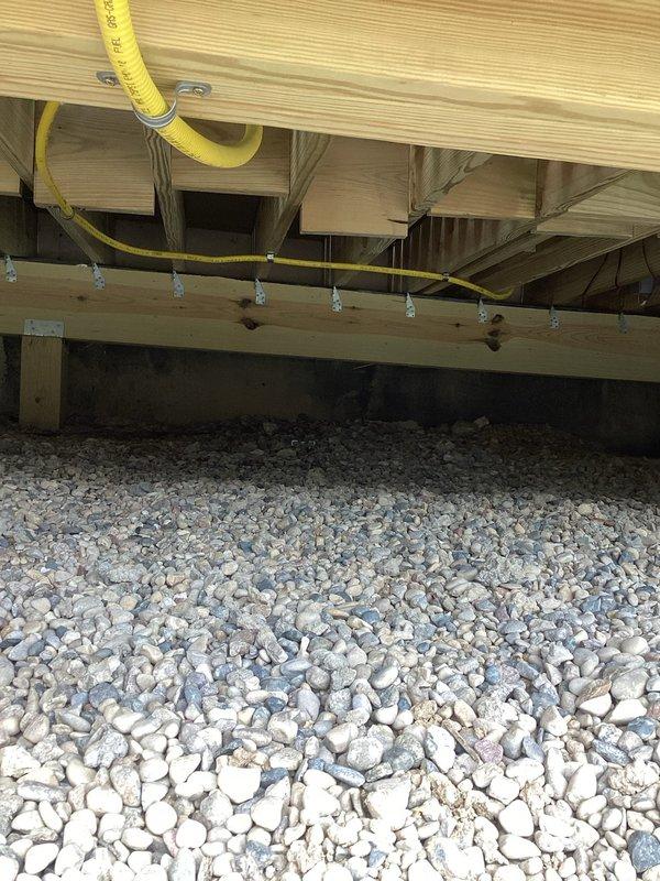 Returned to property to correct gas line installation in crawl space and deck area. Installed proper pipe supports and hangers along floor joists to secure yellow flexible gas line per code requirements. Replaced gas line fittings at deck-mounted connection point, installing new brass fittings and T-joint assembly with proper flanges secured to deck surface. Painted all exposed black iron pipe and fittings throughout installation for corrosion protection and finished appearance.