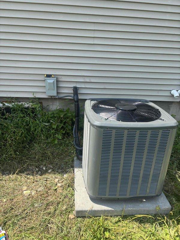 Completed full HVAC system installation including new furnace unit and outdoor air conditioning condenser. Furnace was positioned on black metal base plate in basement mechanical room with proper metallic ductwork connections routed to distribution system throughout residence. Outdoor AC unit was installed on concrete pad against exterior wall with electrical disconnect box mounted to siding, refrigerant lines and electrical connections completed per manufacturer specifications. All components tested and verified operational, system ready for service.
