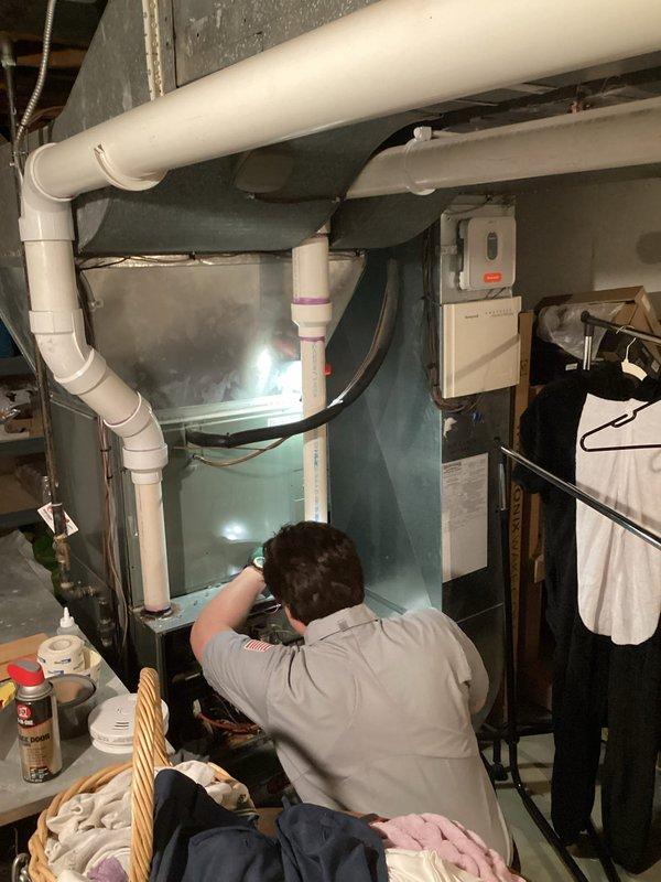 Completed annual cooling maintenance on 20-year-old Rheem system with 2023 condenser model. Performed comprehensive tune-up including indoor air handler inspection in basement utility area and outdoor condenser unit evaluation. Noted significant vegetation overgrowth around outdoor unit restricting airflow and potential for reduced efficiency; condenser accessible but surrounded by ivy, tall grasses, and saplings requiring clearance for proper operation. Inspected condensate drainage system with white PVC piping and verified proper flow. Checked electrical connections at indoor unit with turquoise cabinet panel and verified system operation. Applied lubricant to moving components as needed during maintenance procedure. System currently operational following tune-up protocol.