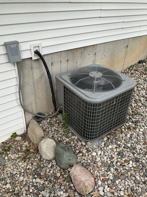 Conducted sales estimate for air conditioning system installation at residential property with existing outdoor condenser unit positioned on gravel bed against exterior wall with vinyl siding. Customer previously purchased furnace and requested mid-range AC system pricing, expressing intent to proceed with installation scheduled for later in the week. Documented existing HVAC equipment setup including electrical disconnect box, conduit connections, and foundation placement for proper system sizing and installation planning.